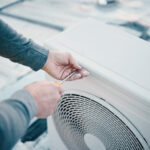 Dłonie mężczyzny rozkręcającego obudowę klimatyzatora śrubokrętem w celu konserwacji i czyszczenia.